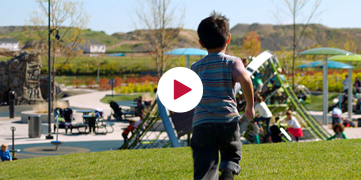 Boy running away from camera to a playground with a Crab Trap climber. A white circle sits in the center of the image with a red triangle looking like a play button.