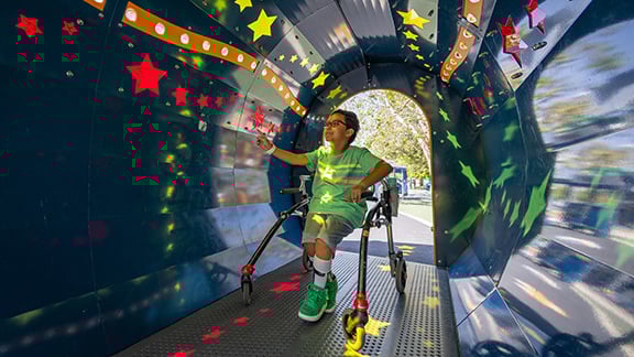 Child on a mobility structure touching the walls of a sensory tunnel.