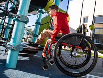 A boy in a wheelchair prepares to transfer to a playground deck