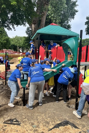 Several community members wearing blue "KABOOM!" t-shirts work together to construct a playground slide. 