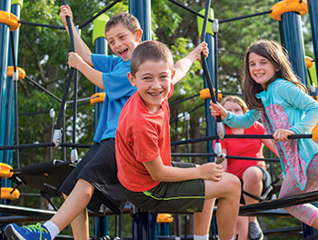 Children smiling while sitting on cable net structure shows social skills in developmental play
