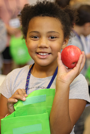 Young girl holding up an apple.